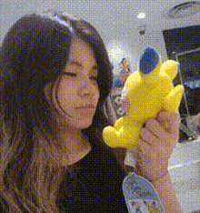a woman is holding a yellow teddy bear in her hands