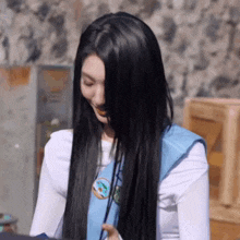 a woman with long black hair is wearing a blue sash around her neck .