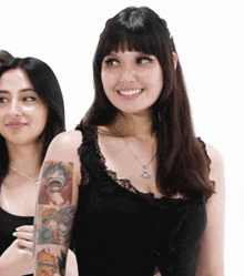 a woman with a tattoo on her arm is smiling and wearing a black tank top