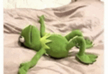 a stuffed kermit the frog is laying on its back on a bed .