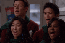 a group of people singing in front of a sign that says ' christmas ' on it