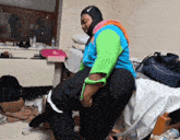 a woman wearing a nike head scarf sits on a man 's lap in a messy room