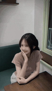 a young girl sits at a table with her hand on her face