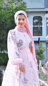a woman wearing a pink hijab and a white dress is standing in front of a building