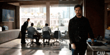a man in a black jacket is standing in front of a cw logo