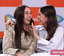 two women are hugging each other in front of a sign that says " wetvsen "