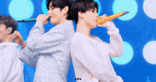 two men singing into microphones while standing back to back on a stage