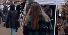 a woman in a green and black plaid shirt is walking in a crowded street .