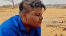 a young man in a blue shirt is sitting on the ground in a desert .