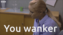 a woman in a blue shirt is sitting in front of a yellow cabinet with the words you wanker written on it