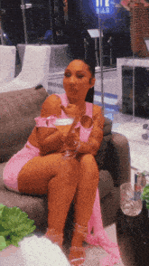 a woman in a pink dress is sitting on a couch holding a glass