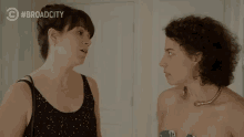 a couple of women standing next to each other with a #broadcity logo behind them