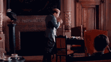 a man in a suit stands in front of a fireplace with a bald eagle on a pedestal