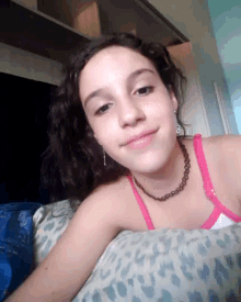 a young girl wearing a pink tank top and a necklace is laying on a bed