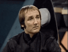 a man in a black shirt is sitting in a chair and looking at something