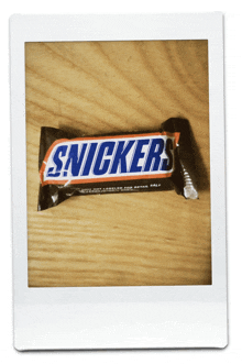 a polaroid of a snickers bar on a wooden surface