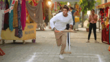 a man in a white shirt is running with a cricket bat in front of a sign that says prishtia
