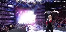 a female wrestler is holding a championship belt over her head in front of a crowd ..