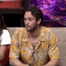 a man in a yellow shirt is sitting on a couch with a microphone in his mouth .