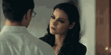 a man and a woman are looking at each other in a room . the woman is wearing glasses and a necklace .