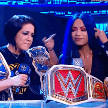 two women are standing next to each other holding a wrestling championship belt with the letter w on it