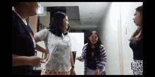 three girls are standing in a hallway talking to each other .