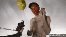 a shirtless man with a red mask on his face is holding a balloon and a can of soda .
