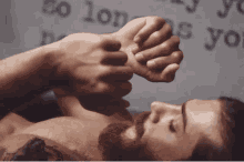 a man with a beard is holding another man 's hand while laying down