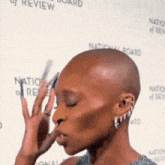 a woman with a shaved head is standing in front of a national board of review banner