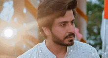 a man with a beard is wearing a white shirt and looking at the camera .