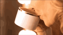 a woman is drinking from a white cup with gold trim