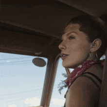 a woman wearing a red bandana and hoop earrings looks out of a car window