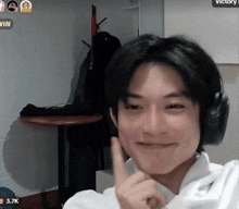 a man wearing headphones and a white shirt is smiling and giving a peace sign