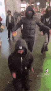 a group of people wearing masks and hoodies are dancing in a crowded street .