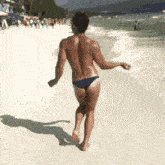 a shirtless man in a blue bikini is walking along a beach .