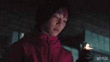 a woman in a red jacket is holding a lighter with netflix written on the bottom right