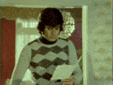 a man in a plaid sweater holds a piece of paper in his hand