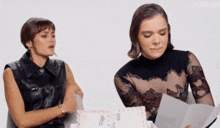 two women are sitting next to each other and one of them is holding a piece of paper .