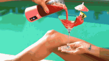 a person pouring a drink into a martini glass with an umbrella