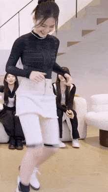 a woman in a black top and white skirt is dancing in a living room