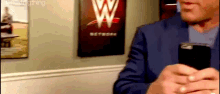 a man in a suit is holding a cell phone in front of a wall with a wwe logo on it .