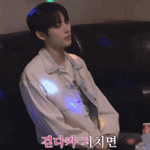 a man in a white jacket sits on a couch with korean writing on the wall