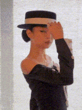 a woman wearing a black hat and a black dress is covering her face with her hand .
