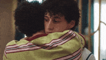 two young men are hugging each other and one has curly hair