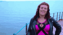 a woman in a pink top and black jacket is standing in front of the ocean