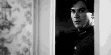 a black and white photo of a man standing in a doorway looking out .