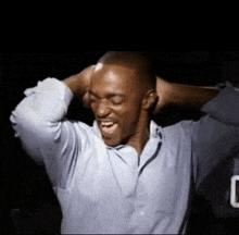 a man in a blue shirt is holding his hands to his head and smiling