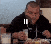 a man is sitting at a table eating a meal with a spoon and fork .