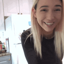 a woman in a black shirt is smiling in front of a white refrigerator