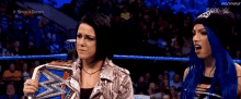 two women are standing in a wrestling ring and one is holding a wrestling championship belt .